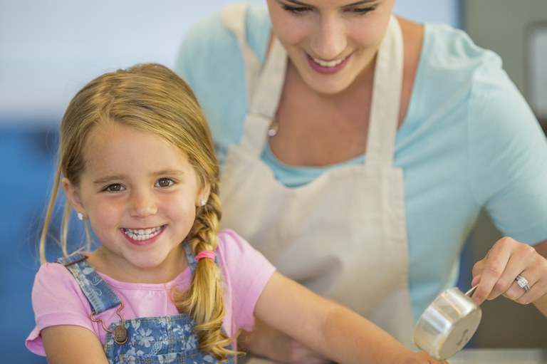 Girl with woman in kitchen measuring ingredients 