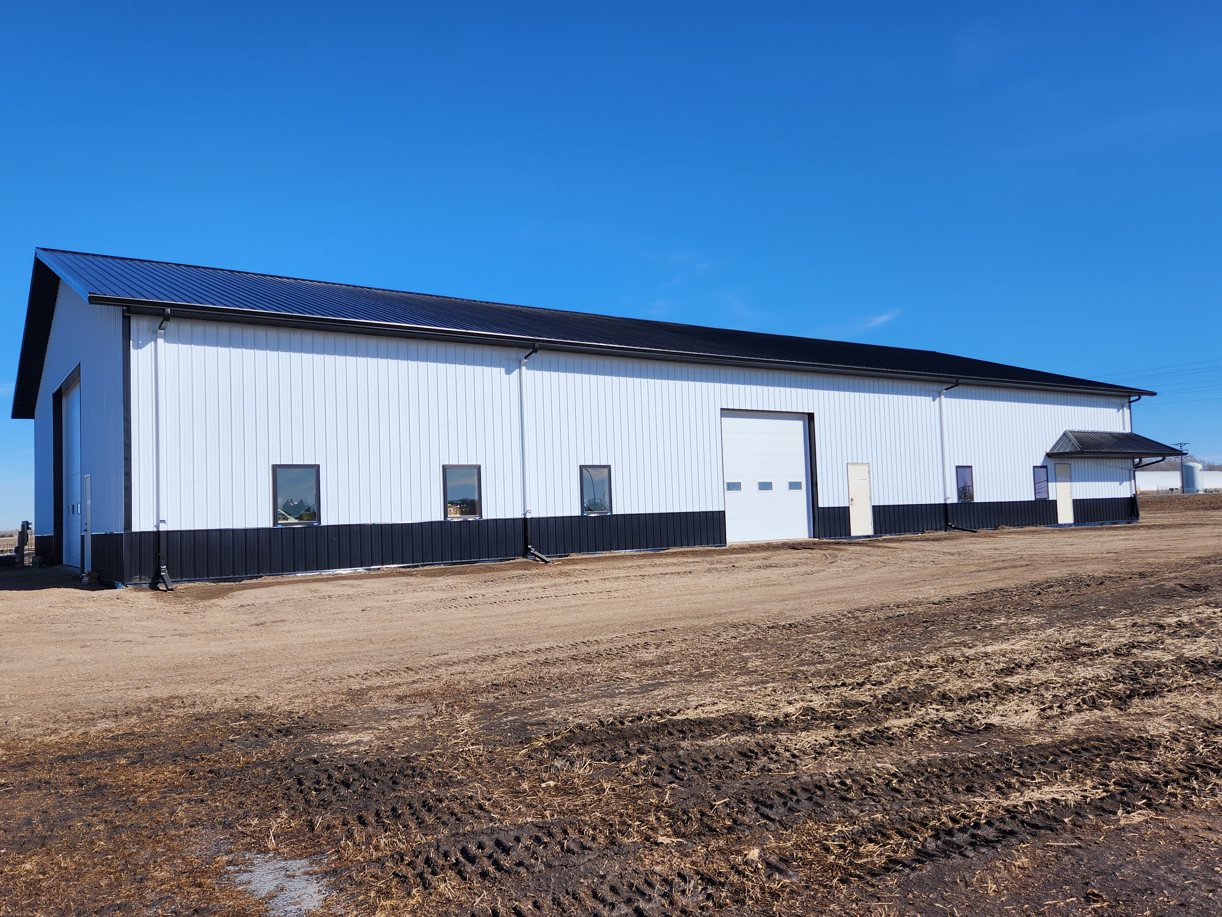 A 65x120-foot steel building with black wainscotting, white side walls, and a black roof stands on a gravel yard at the NDSU Oakes Irrigation Site.
