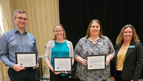 A woman poses with two woman and a man with award certificates