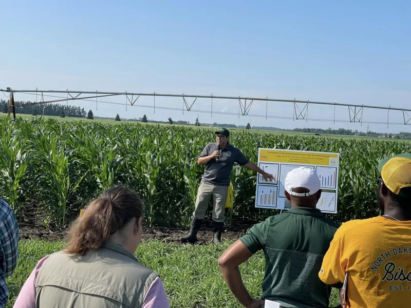 Man presenting information to a crowd in front of a field with irrigation sprayers
